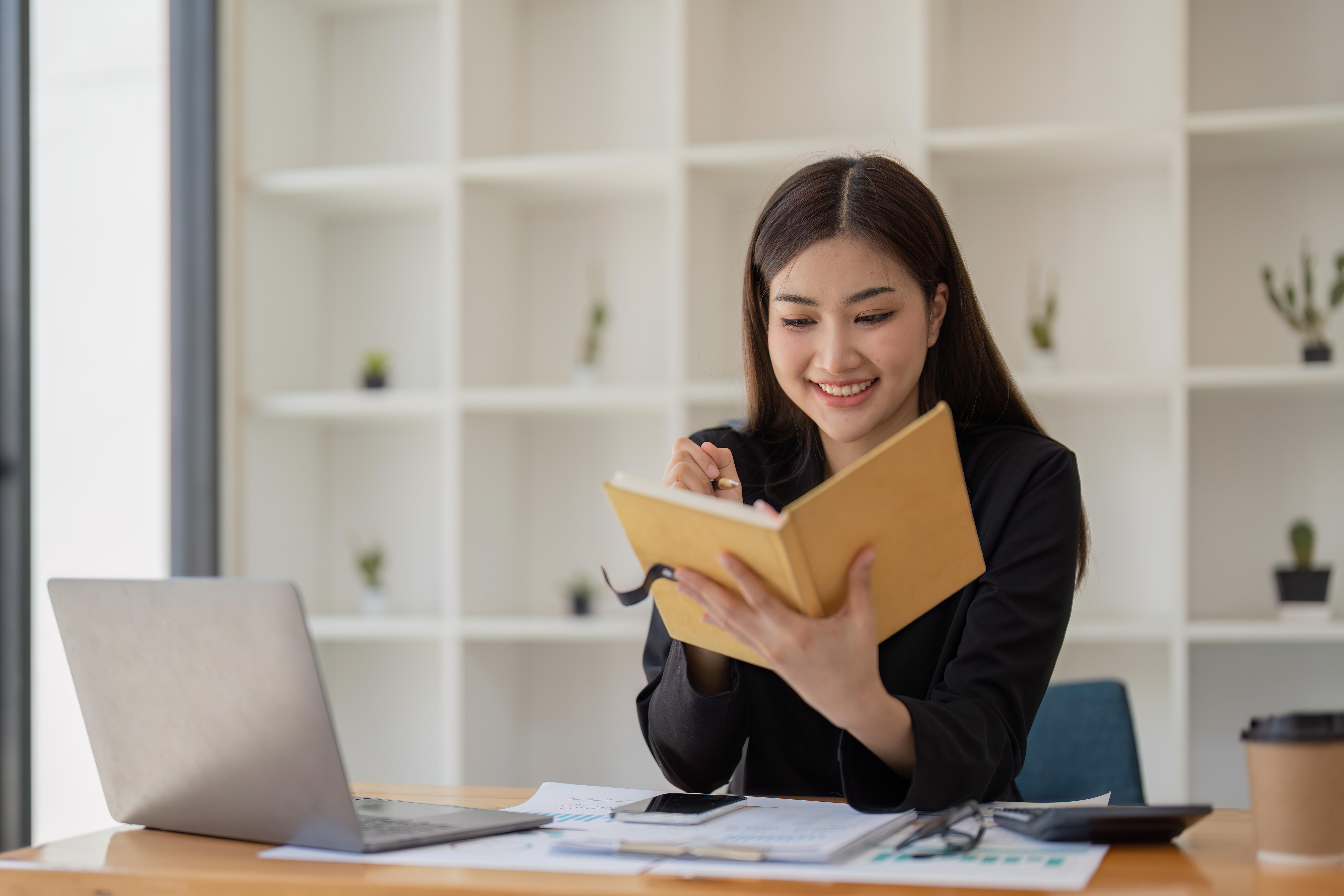 Focused Asian female accountant or financial analyst at laptop screen and taking notes