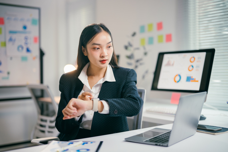 Businesswoman checking the time on her smartwatch while working on a laptop in a modern office